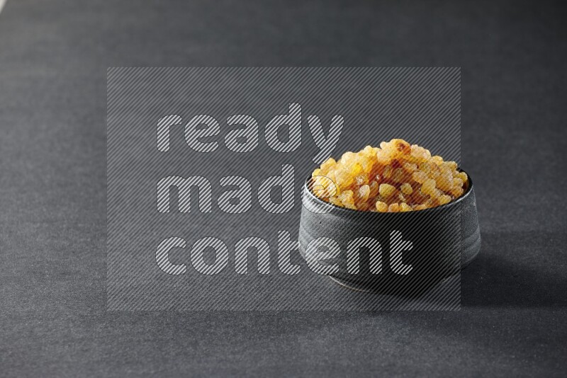 A black pottery bowl full of raisins on a black background in different angles