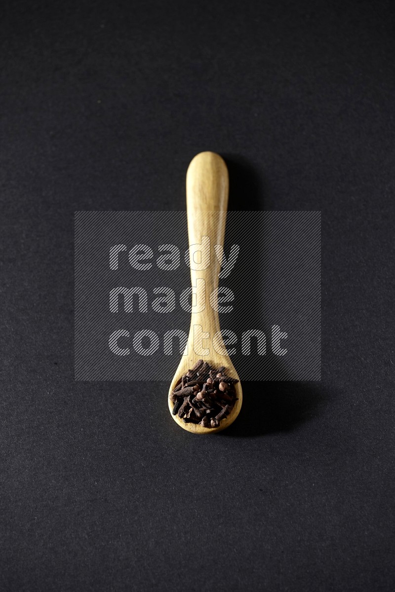 A wooden spoon full of cloves on a black flooring
