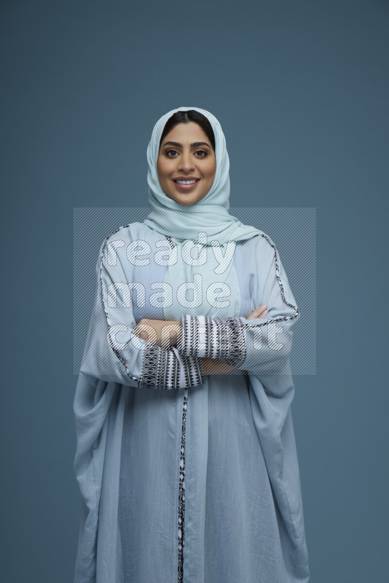 A woman posing in a blue background wearing a blue Abaya with hijab