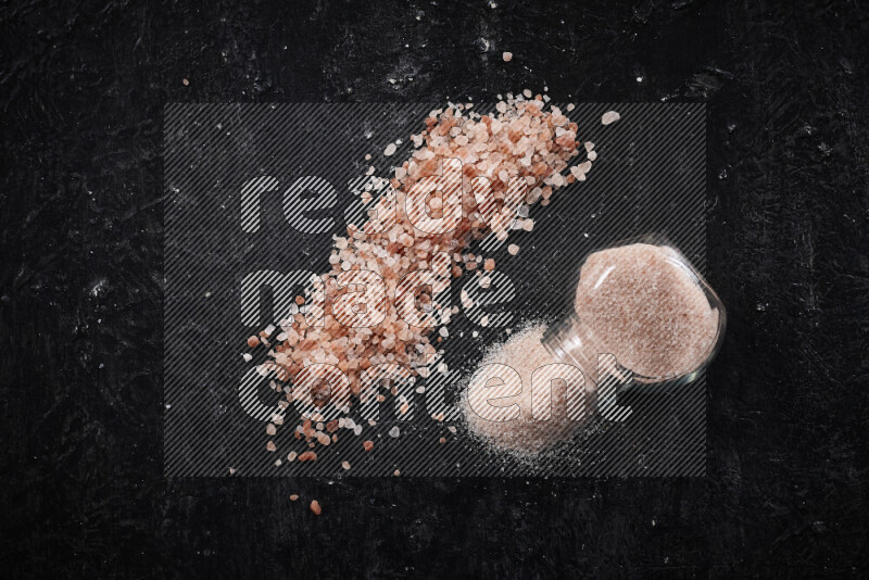 A glass jar full of fine himalayan salt with some himalayan crystals beside it on a black background