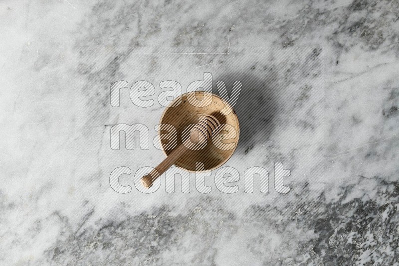 Beige Pottery Bowl with wooden honey handle in it, on grey marble flooring, Top View