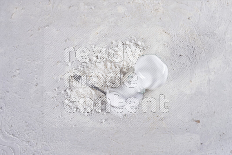 A glass jar full of table salt with some sea salt crystals beside it on a white background