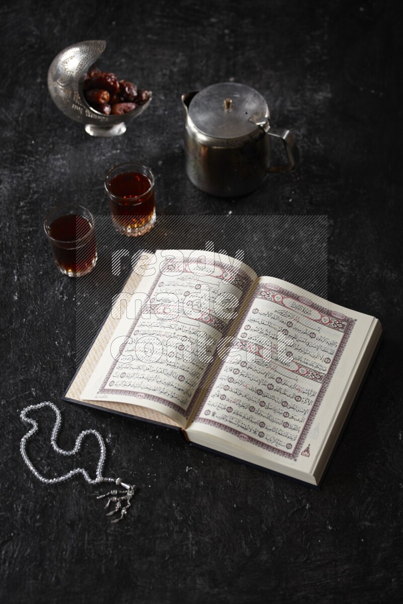 مصحف مع فناجين شاي وسبحة علي خلفية سوداء خشبية