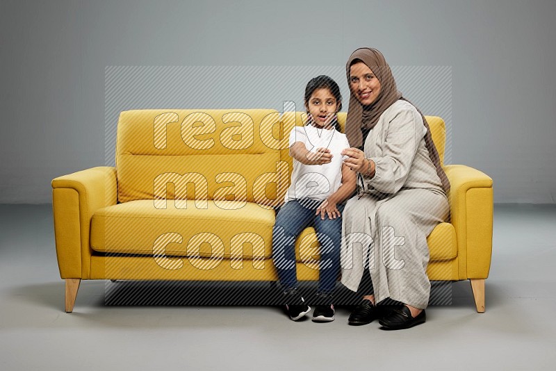 Mom and daughter sitting on sofa holding ATM card on gray background