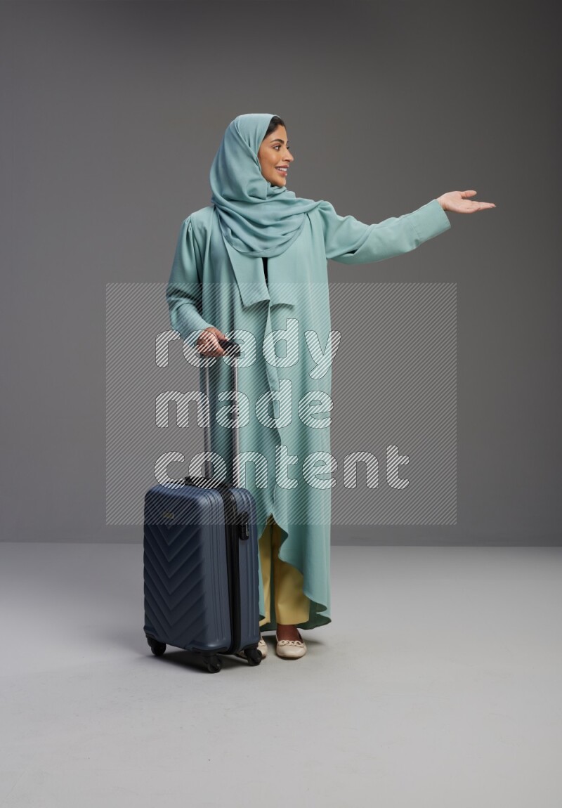 Saudi Woman wearing Abaya standing holding Travel bag on Gray background