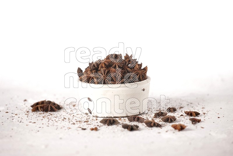 Star Anise in a white bowl and more of it sprinkled on white background