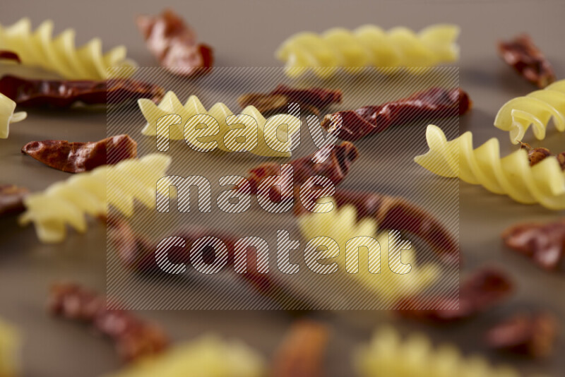 Raw pasta with different ingredients such as cherry tomatoes, garlic, onions, red chilis, black pepper, white pepper, bay laurel leaves, rosemary and cardamom on beige background