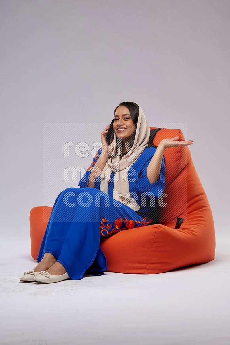 A Saudi woman wearing Jalabiya sitting on an orange beanbag and talking on the phone