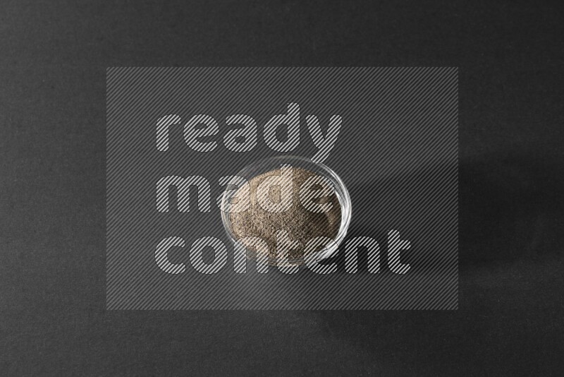 فلفل أسود مطحون في وعاء زجاجي علي خلفية سوداء