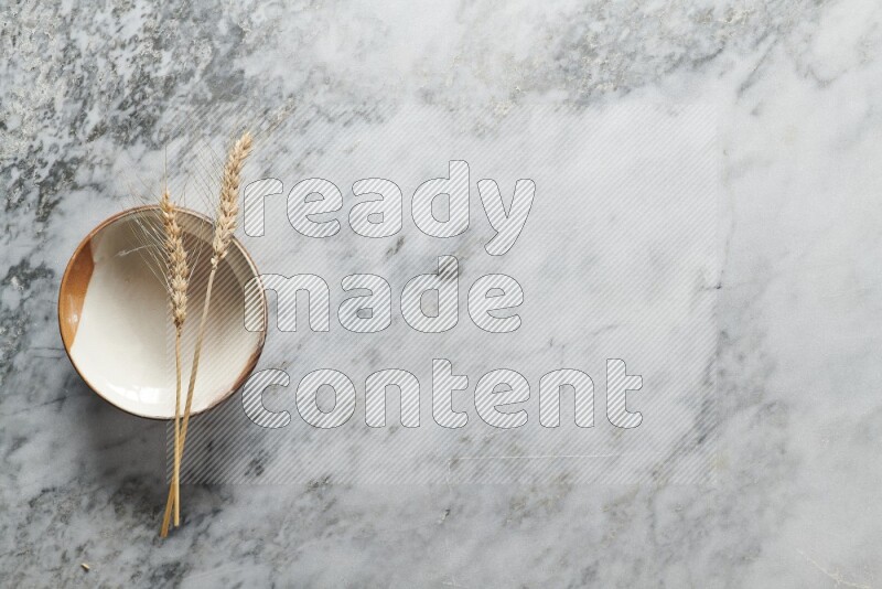 Wheat stalks on multicolored pottery plate on grey marble background
