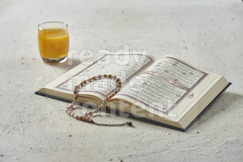Quran with dates, prayer beads and different drinks all placed on textured white background