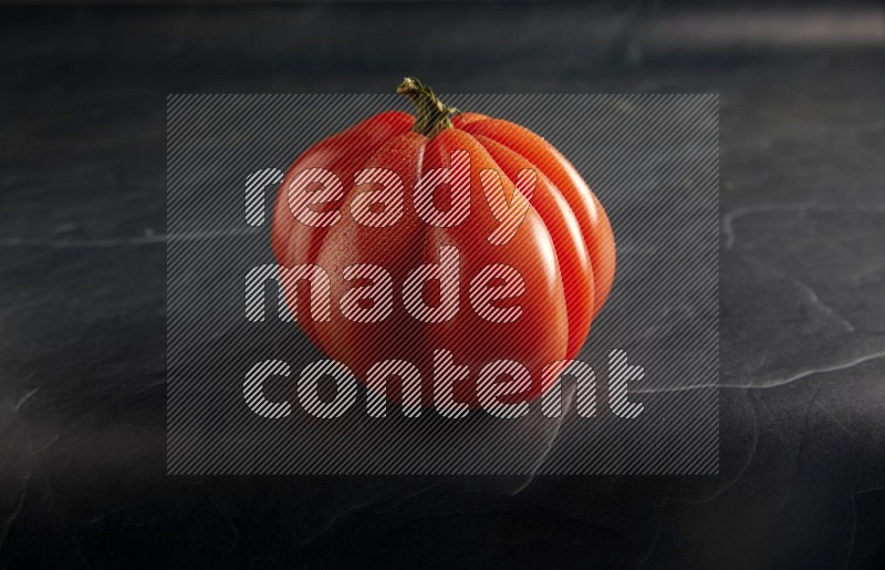 45 degree single heirloom tomato on a textured black slate background