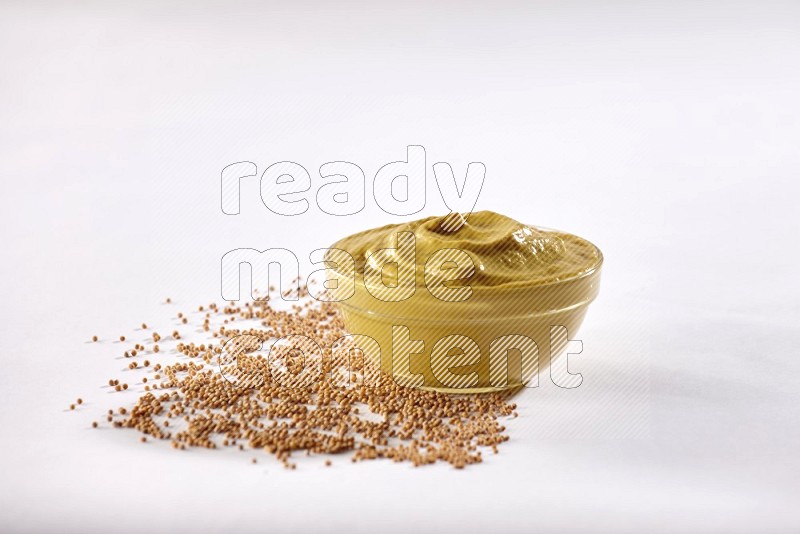 A glass bowl full of mustard paste with mustard seeds underneath on white flooring in different angles