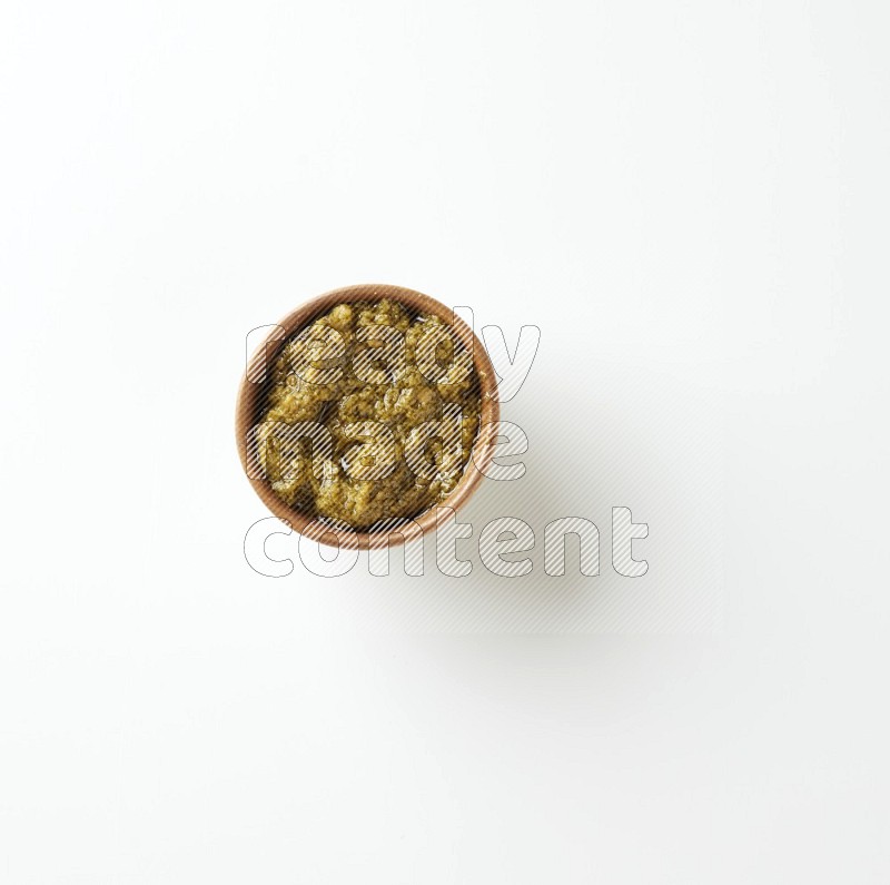 small brown ceramic round bowl filled with pesto paste on a white counter top