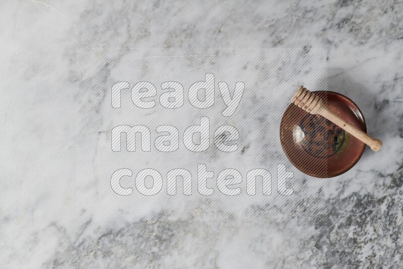 Decorative pottery plate with wooden honey dipper in it on grey marble background