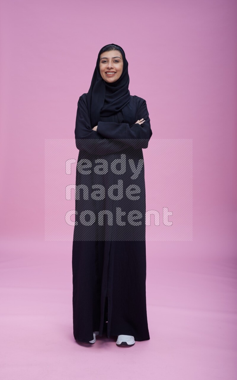 Saudi woman wearing Abaya standing with crossed arms on pink background