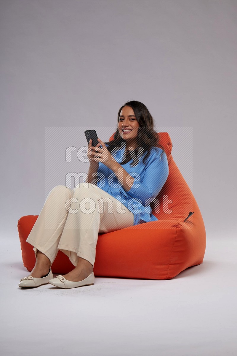 A woman sitting on an orange beanbag and texting on phone