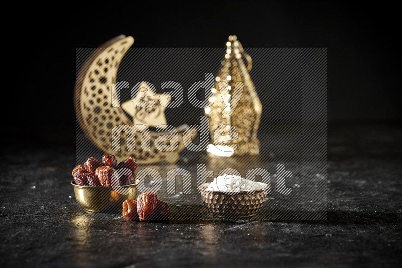 Dates in a metal bowl with desiccated coconuts beside golden lanterns in a dark setup