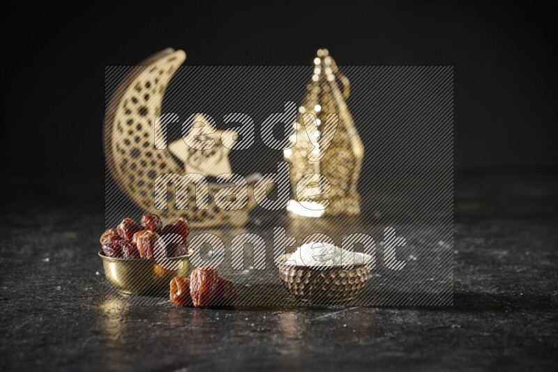 Dates in a metal bowl with desiccated coconuts beside golden lanterns in a dark setup