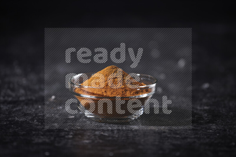 A glass bowl full of ground paprika powder on black background