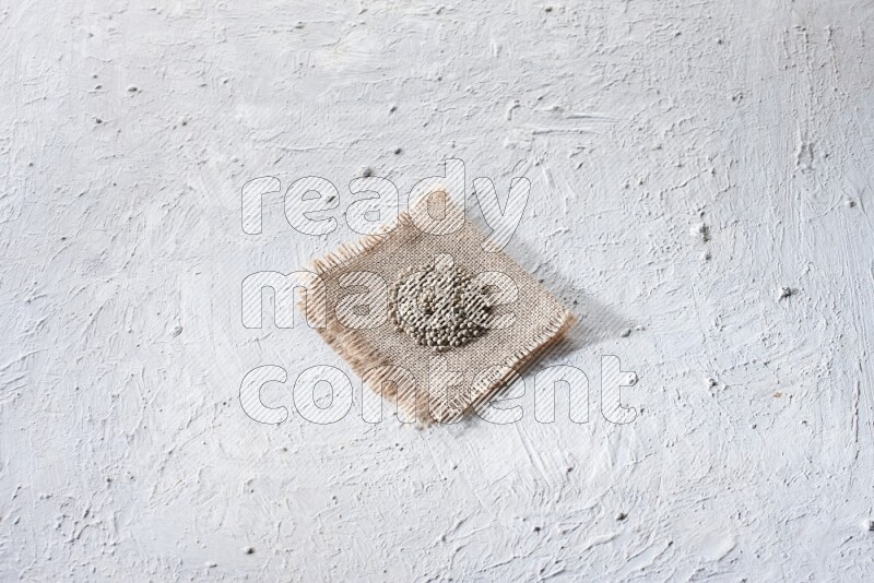 White pepper beads on a burlap piece of fabric on textured white flooring