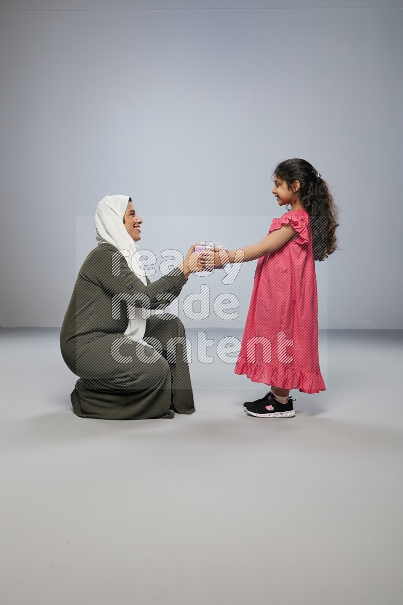 A girl giving a gift to her mother on gray background