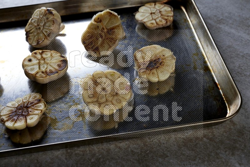 half's roasted garlic in a stainless tray on a grey textured countertop