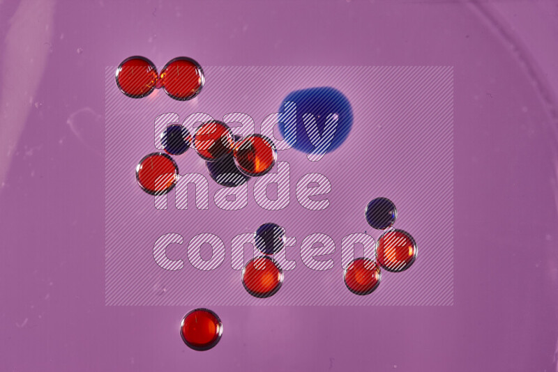 Close-ups of abstract red and blue watercolor drops on oil Surface on pink background