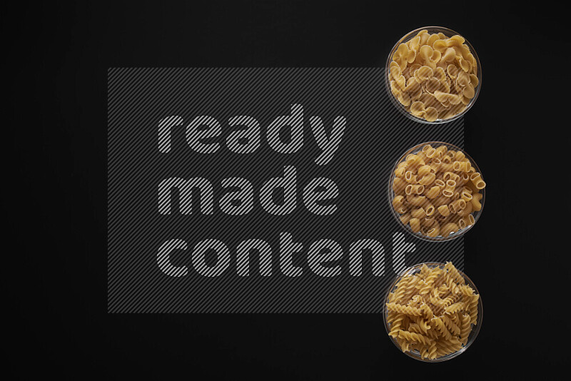 Different pasta types in 3 glass bowls on black background