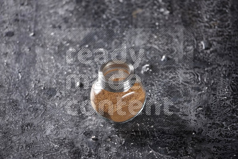 Herbal glass jar full of cinnamon powder on a textured black background