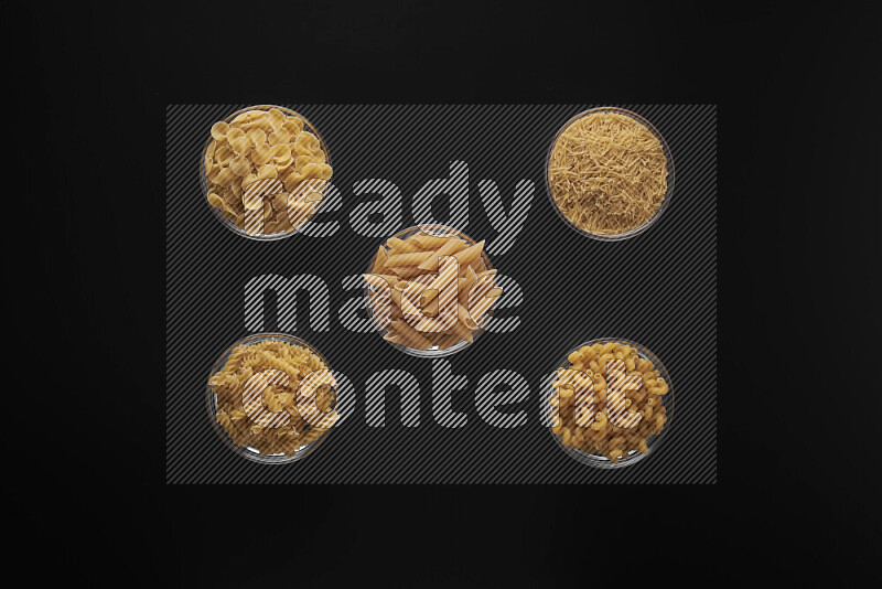 Different pasta types in 5 glass bowls on black background