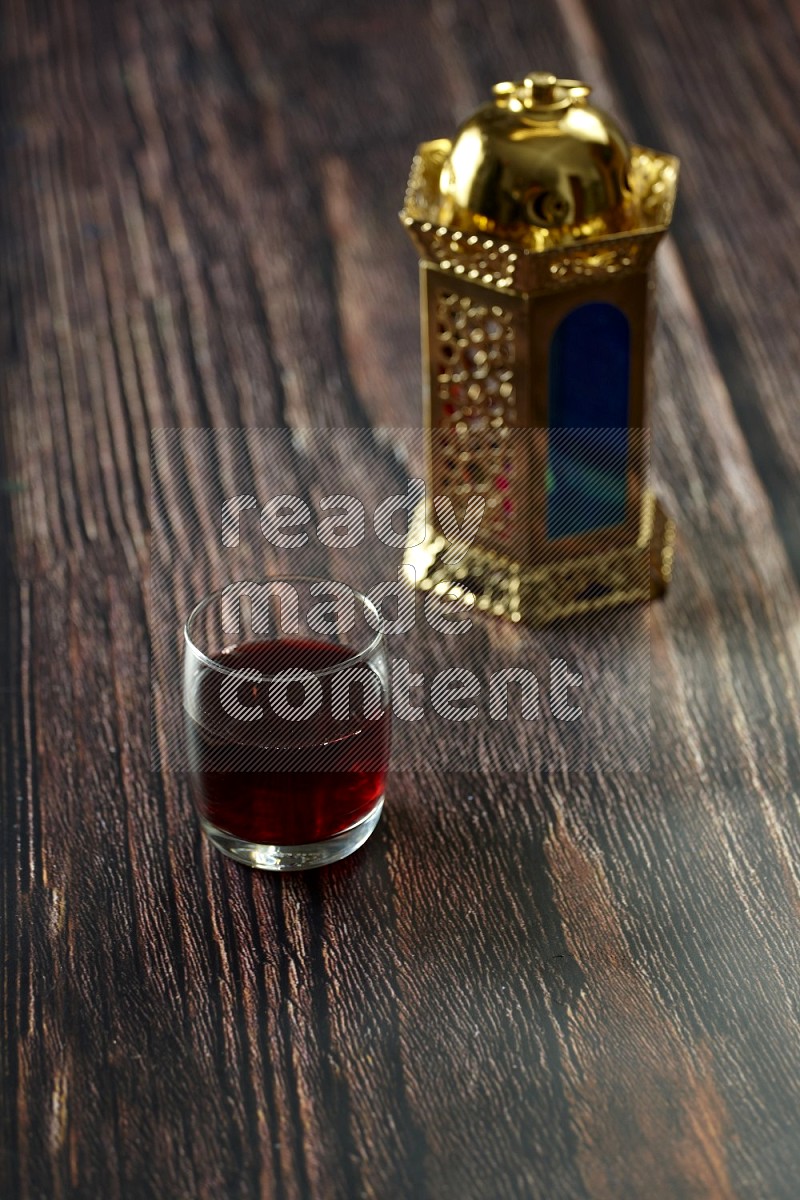 A golden lantern with different drinks, dates, nuts, prayer beads and quran on brown wooden background