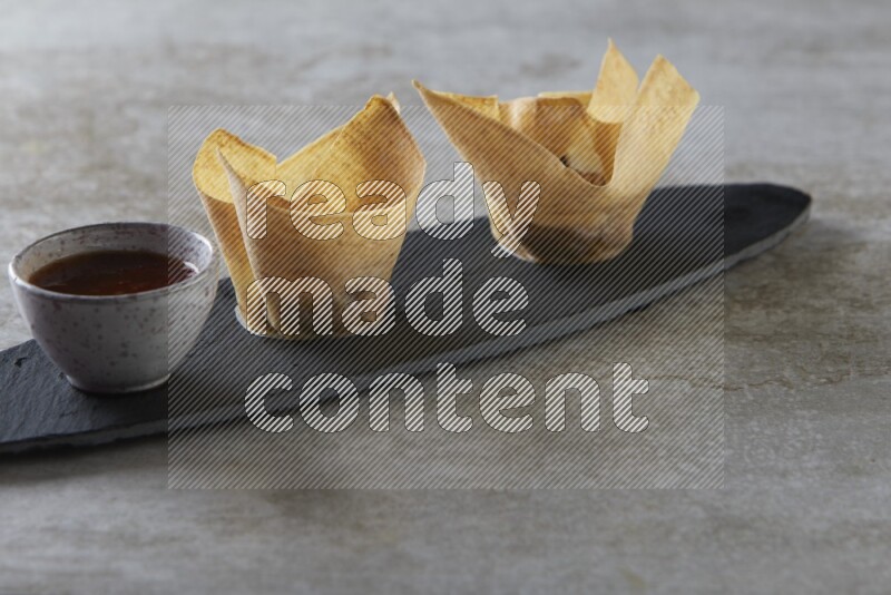 wonton cups with soy sauce ramkin on oval slate on grey textured counter top