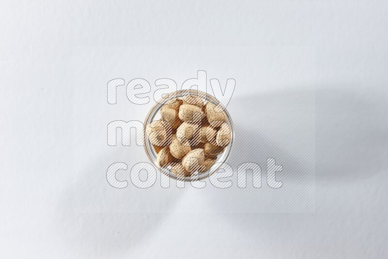 A glass bowl full of almonds on a white background in different angles
