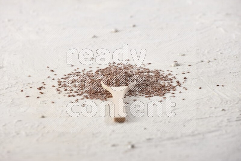 A wooden spoon full of flax seeds surrounded by flax seeds on a textured white flooring