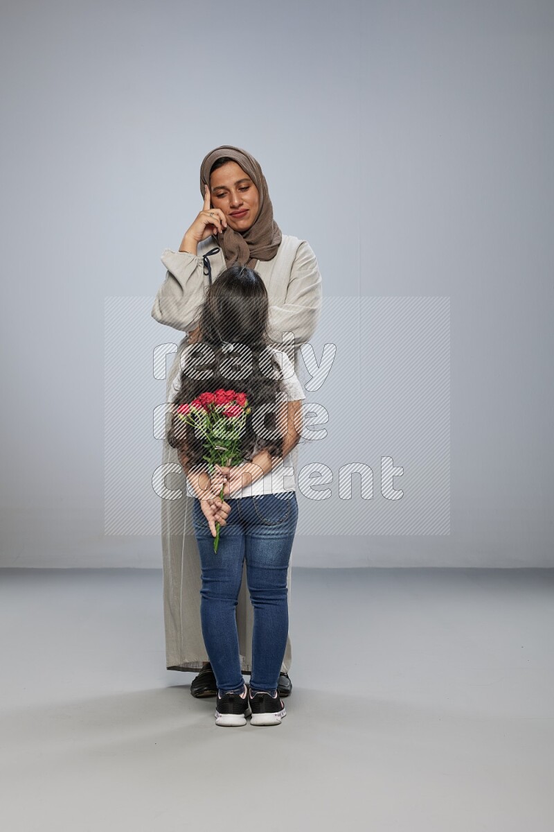 A girl hiding a flower behind her back for her mother on gray background