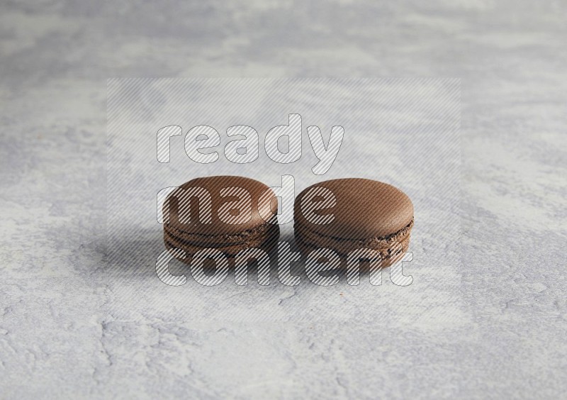 45º Shot of two Brown Dark Chocolate macarons  on white  marble background