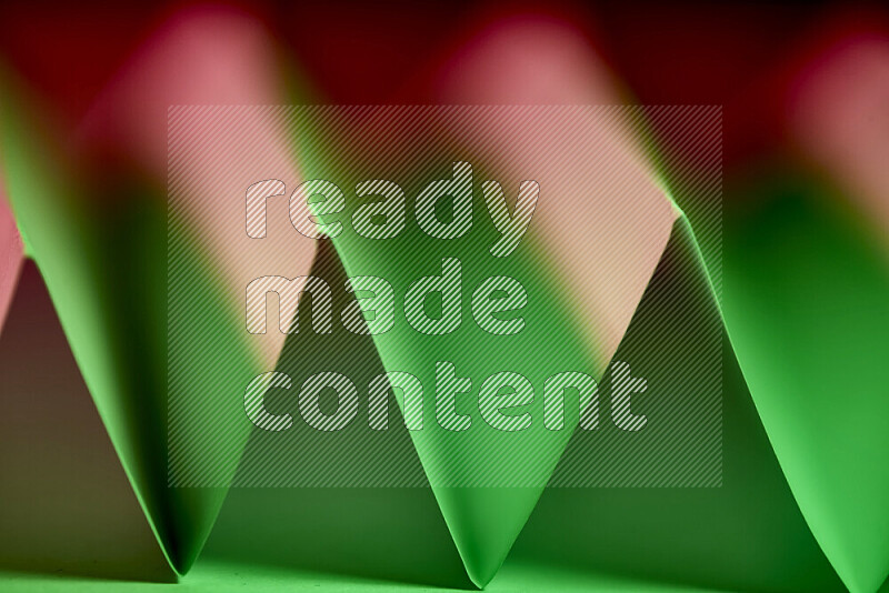 صورة مجردة مقربة تظهر طيات ورقية هندسية حادة بتدرجات اللون الأخضر والأحمر