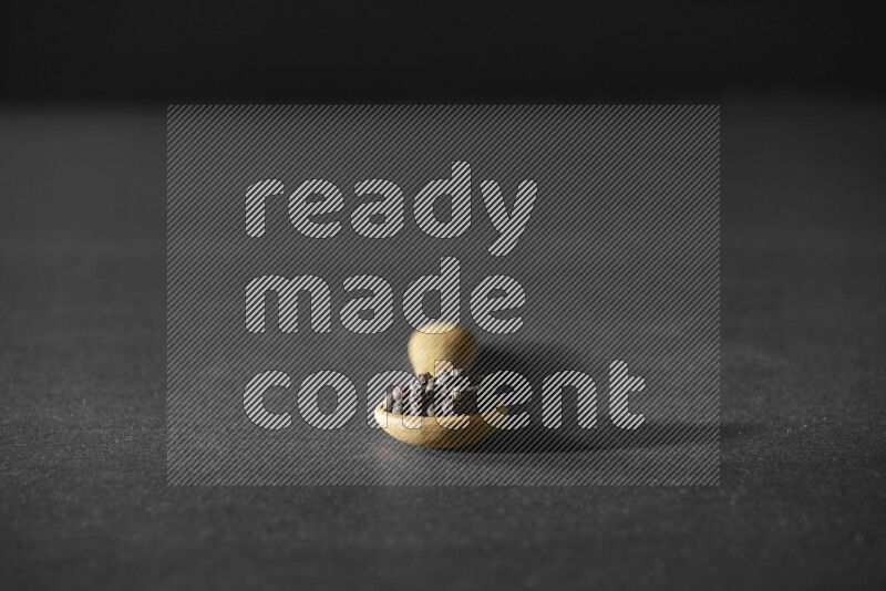 حبوب الفلفل الأسود في ملعقة خشبية علي خلفية سوداء