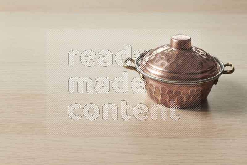 A small copper pot on light wooden background