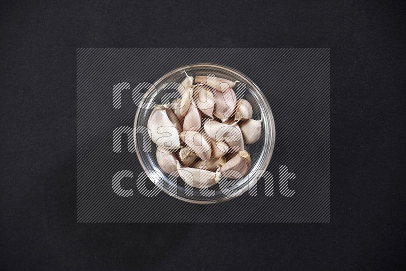 A glass bowl full of garlic cloves on a black flooring in different angles