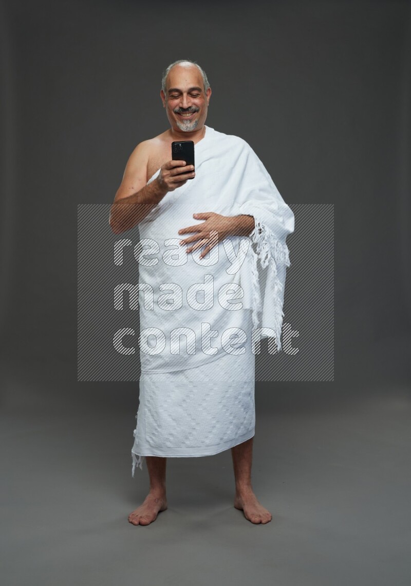 A man wearing Ehram Standing texting on phone on gray background