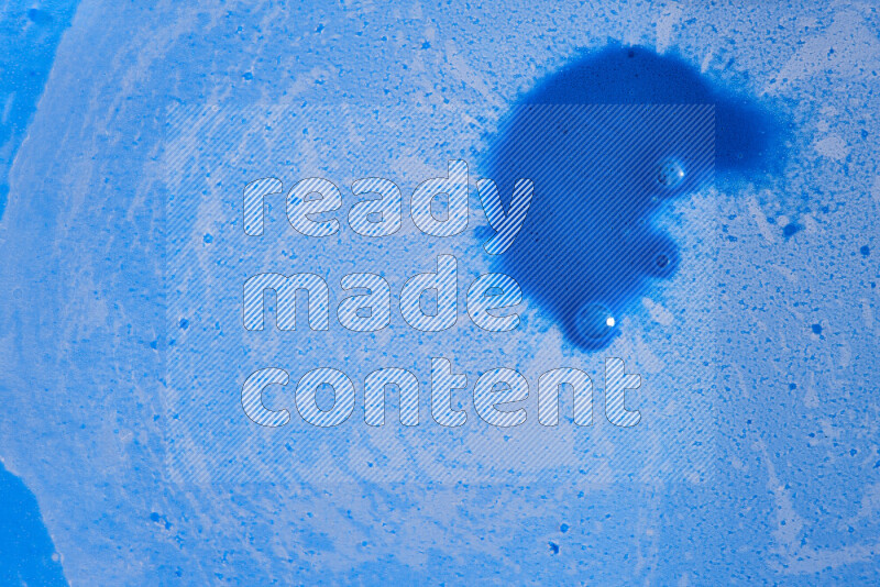 The image captures a dramatic splatter of blue paint over a blue backdrop