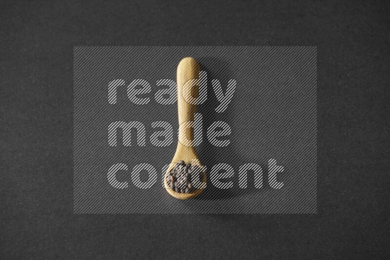 حبوب الفلفل الأسود في ملعقة خشبية علي خلفية سوداء