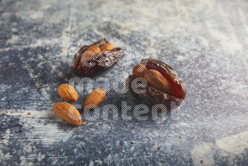 two almond stuffed madjoul dates on a rustic blue background