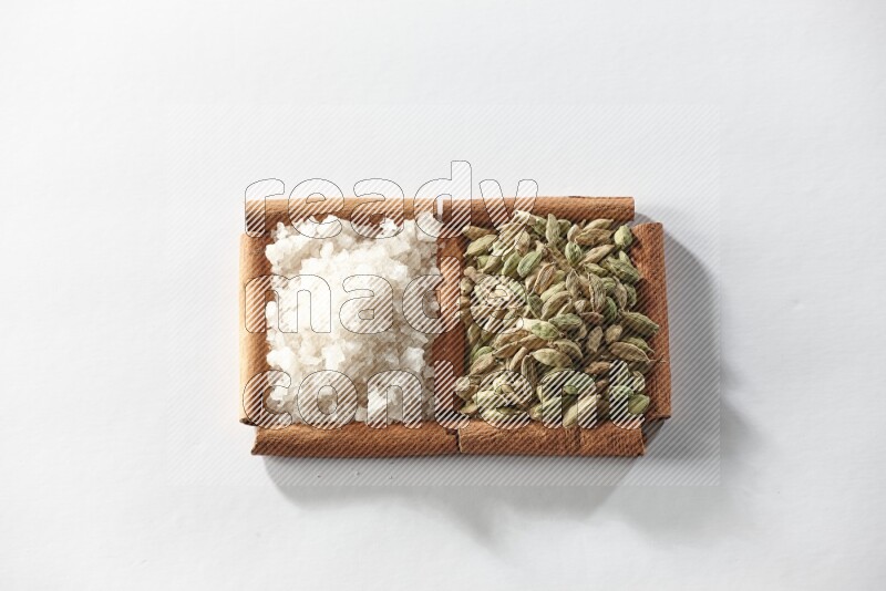 مربعان من أعواد القرفة ممتلئان بحبوب الهيل والملح الأبيض علي خلفية بيضاء