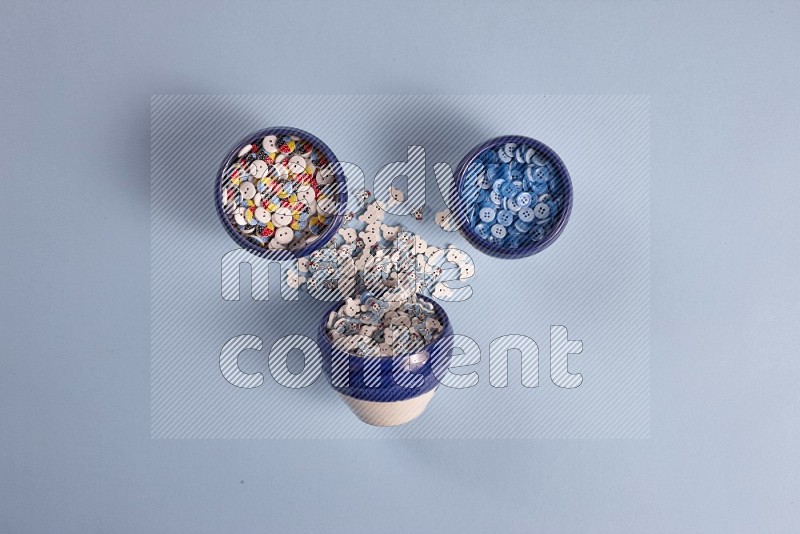 Multicolored pottery bowl full of colored buttons on blue background