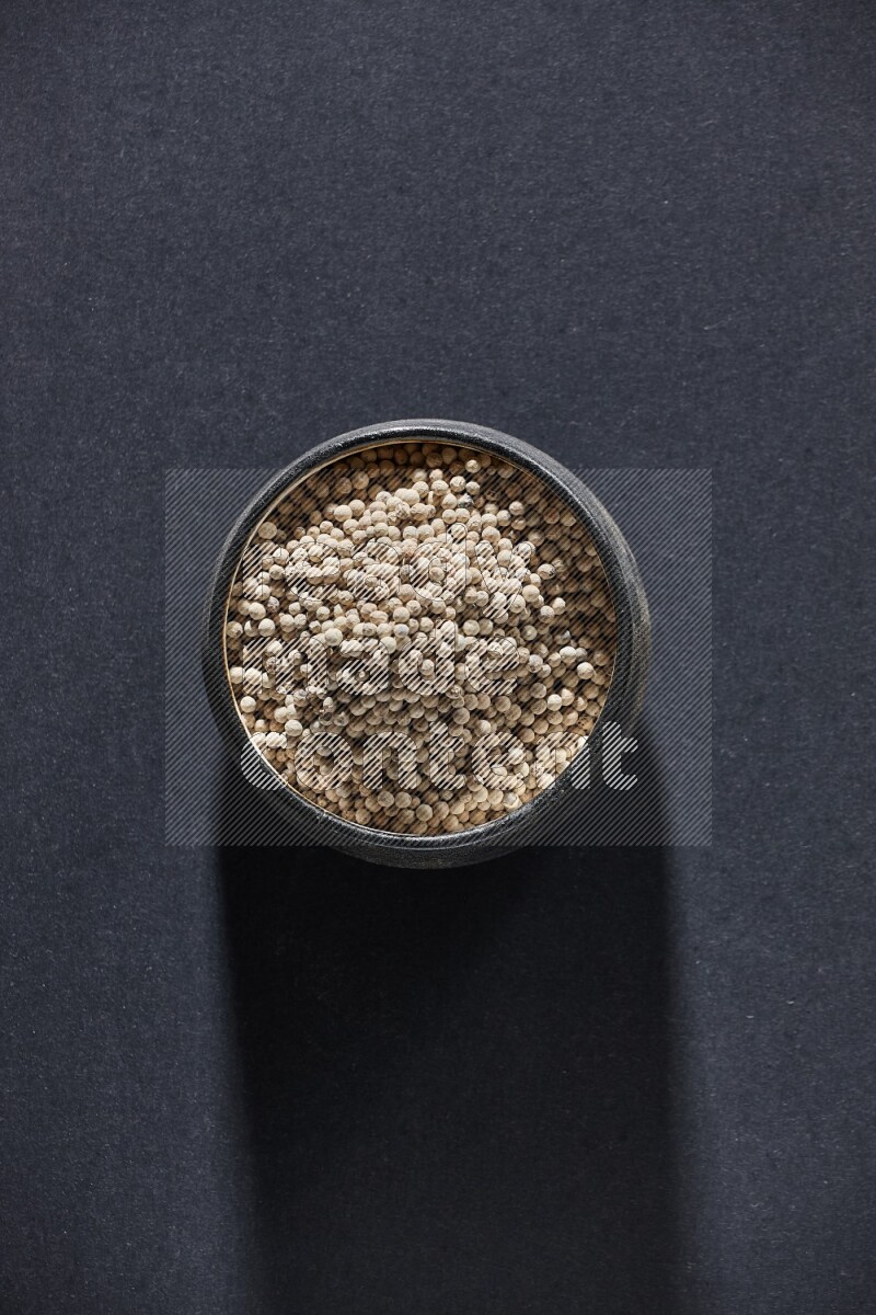 وعاء فخار أسود مملوء بالفلفل الأبيض على أرضية سوداء