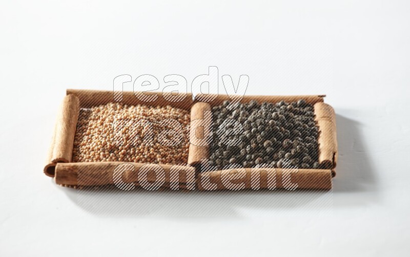 مربعان من أعواد القرفة ممتلئان بحبوب الخردل وحبوب الفلفل الأسود علي خلفية بيضاء