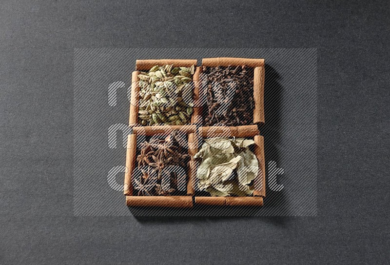 4 squares of cinnamon sticks full of star anise, cardamom, cloves and bay laurel leaves on black flooring